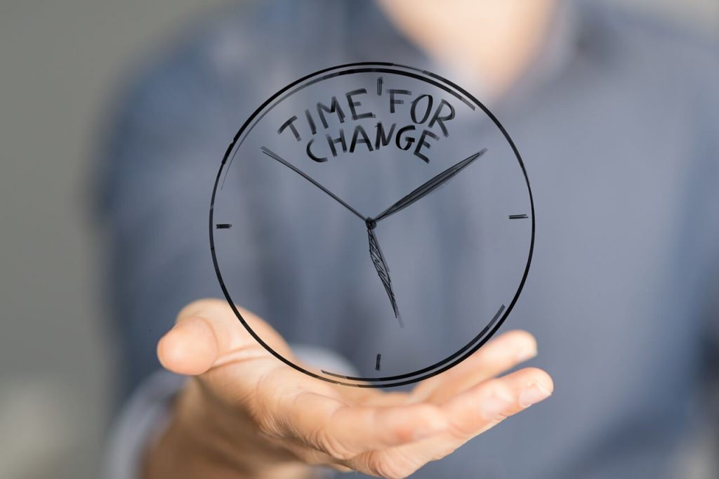 una mano tiene sollevato un orologio disegnato in 3d con scritto time for change