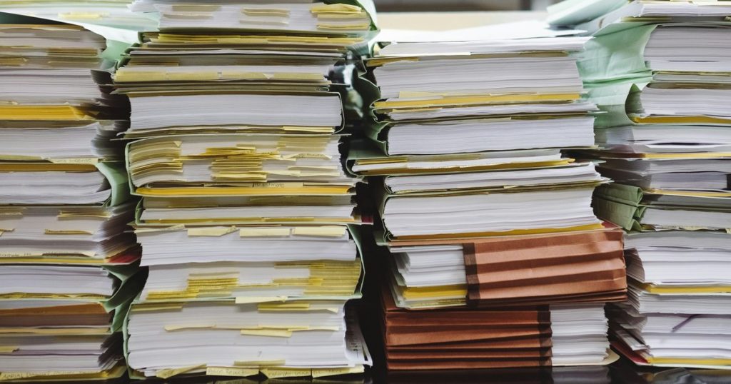 Pile di faldoni e documenti cartacei accatastati su una scrivania